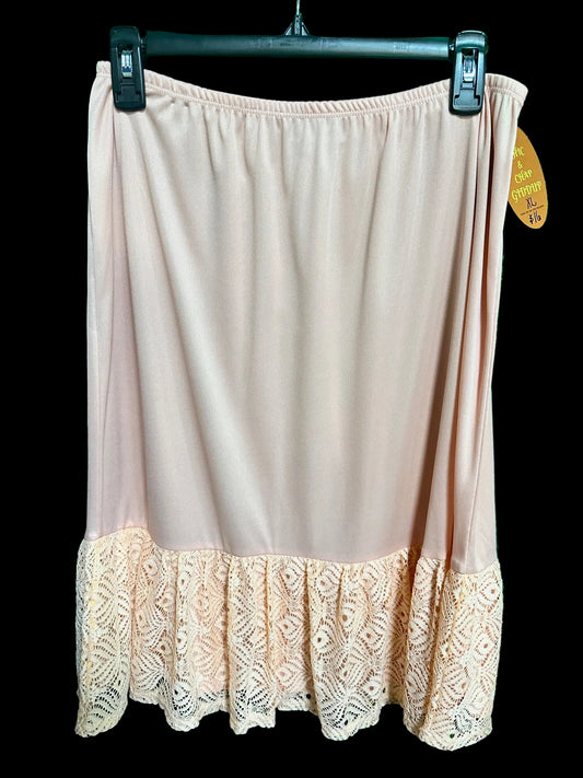 A peach lace slip extender skirt with a solid color upper and lace detailing at the lower edge, displayed on a hanger against a green background.